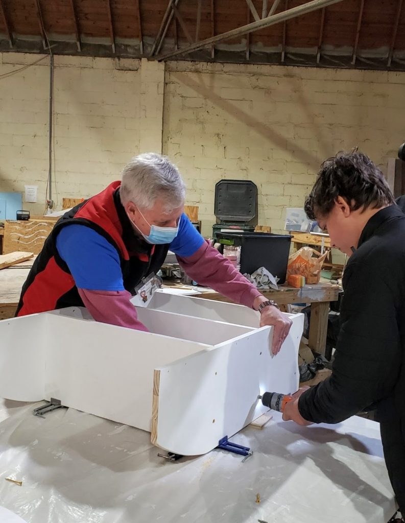 Two individuals work on assembling a bookshelf as part of the Youth Build program.